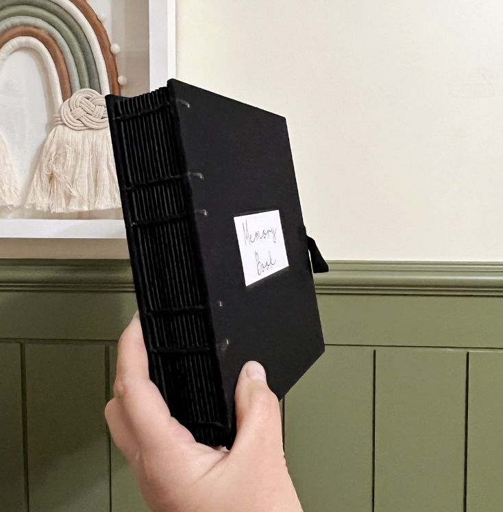 Álbum preto visto em perspectiva, com costura aparente e etiqueta na capa